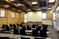 Front of room view with lectern on left,  projection screen lowered, and markerboard on the right