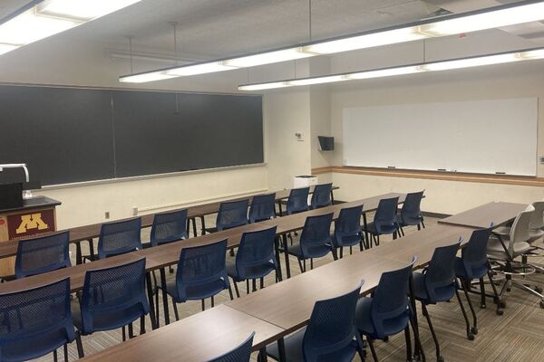 Front of room view with lectern on left in front of chalkboard, projection screen lowered