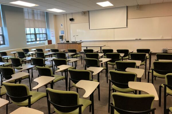 Front of room view with lectern on left in front of markerboard and projection screen partially lowered