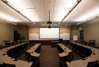 View from Audience back middle of classroom with displays showing 1) instructor slides. 2) a view of the instructor, camera that focuses on instructor and class member seating arrangement