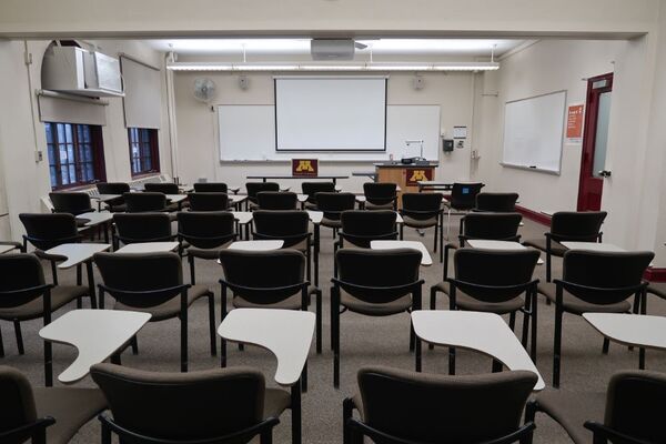 Front of room view with lectern on right in front of markerboard and projection screen lowered, exit door on right 