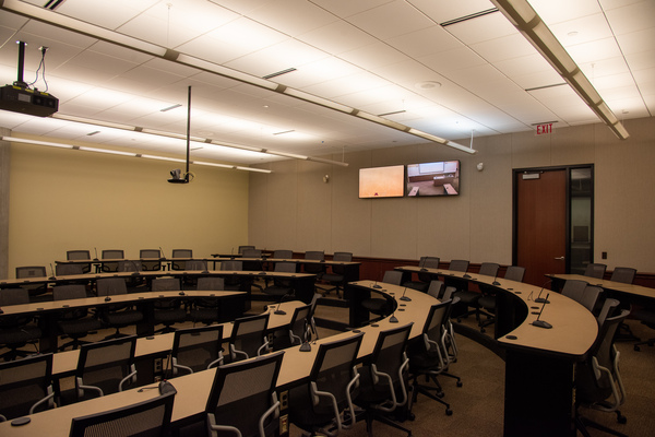 View from audience left side perspective looking towards rear of classroom showing rear exit door, instructor camera, rear self view monitors, and audience seating