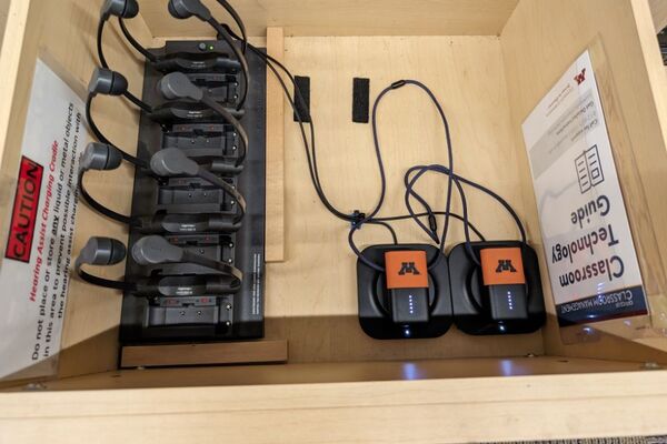 Pedestal - inside view of drawer showing two wireless mics in charging base and assistive listening devices in charger