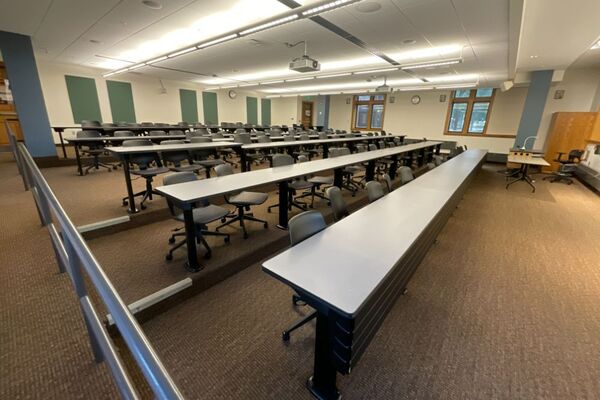 Back of room view of student tiered fixed-table and chair seating and exit doors at left and right rear of room