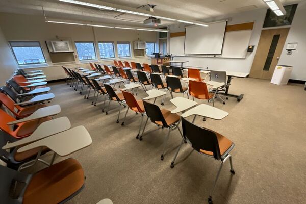 Front of room view with lectern on left in front of markerboard and projection screen lowered