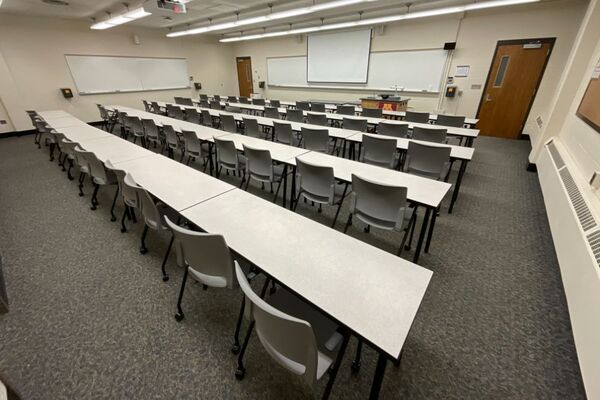 Front of room view with lectern on right in front of markerboard and projection screen partially raised