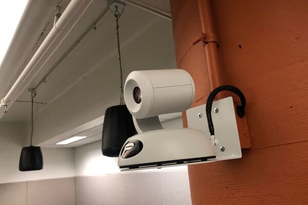 Camera mounted to a wall and instructor enabled adjustments to the lens to allow the instructor to be "seen" by the camera in more locations around the room