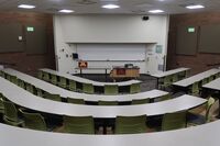 Front of room view with lectern center in front of markerboard and projection screen above, exit doors to left and right