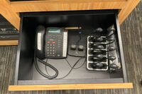 Pedestal - inside view of drawer showing two wireless mics in charging base, telephone, and assistive listening devices in charger