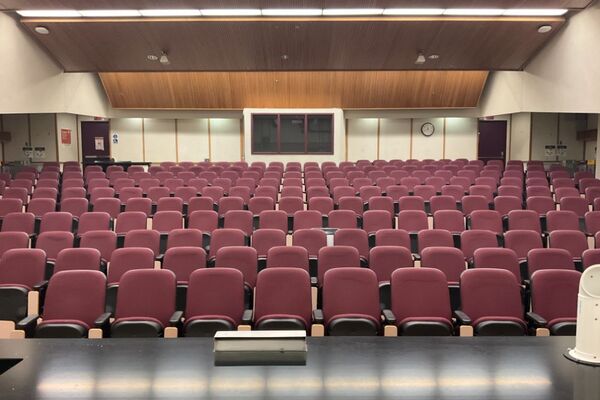 Back of room view of student auditorium seating, A/V booth center, and exit doors at rear of room