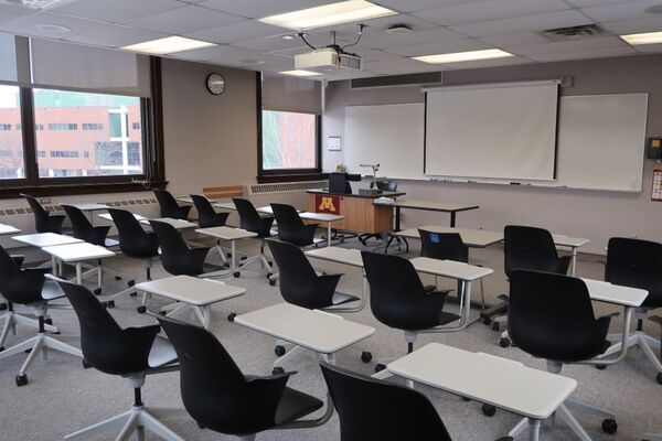 Front of room view with lectern on left in front of markerboard and projection screen lowered