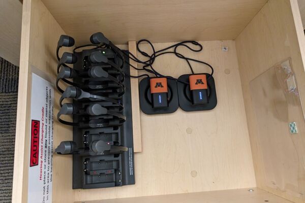 Pedestal - inside view of drawer showing two wireless mics in charging base, and assistive listening devices in charger