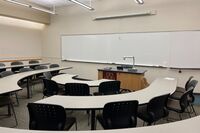 Front of room view with lectern on center in front of markerboard and projection screen lowered