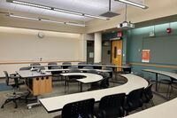 Back of room view of student tiered fixed-table and chair seating and tackboard on back wall